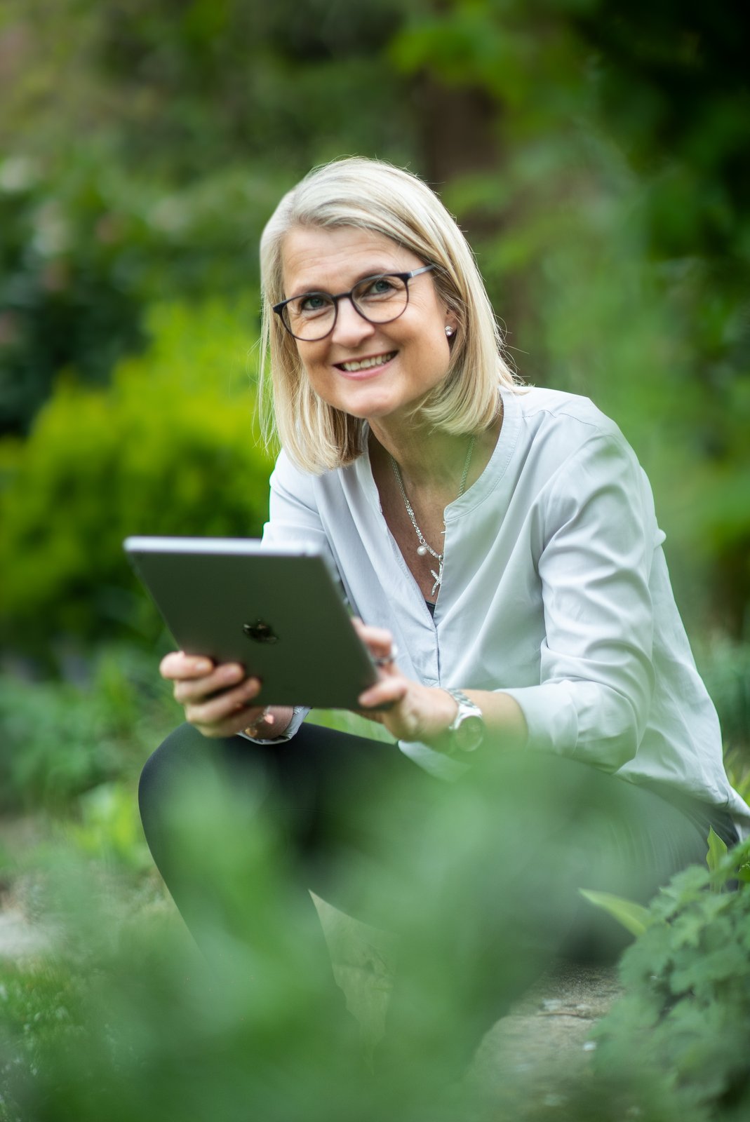 Angela Rakowitz lächelnd mit Tablet im Garten